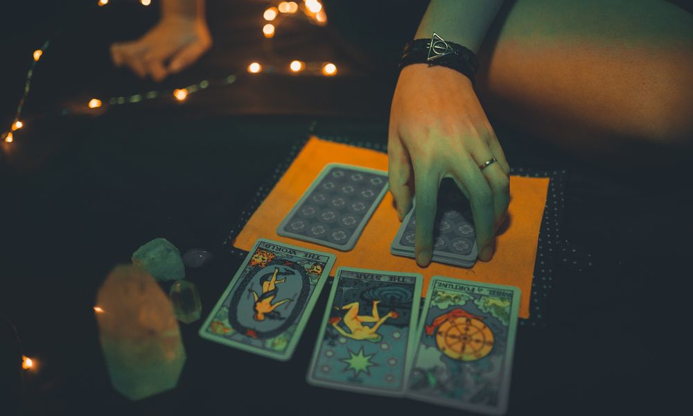 A hand laying out a three-card tarot spread on a dark cloth by candlelight, a daily practice that pairs with a fixed major arcana destiny matrix chart