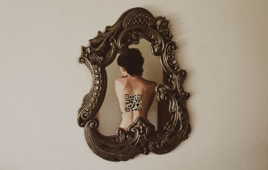 Back view faceless female bare back with black barcode reflecting in cozy mirror with unusual creative frame hanging on plain light pink wall