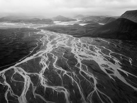 Distance black and white scenery of rough mountainous terrain with breathtaking pattern of glacier frozen rivers under cloudy sky
