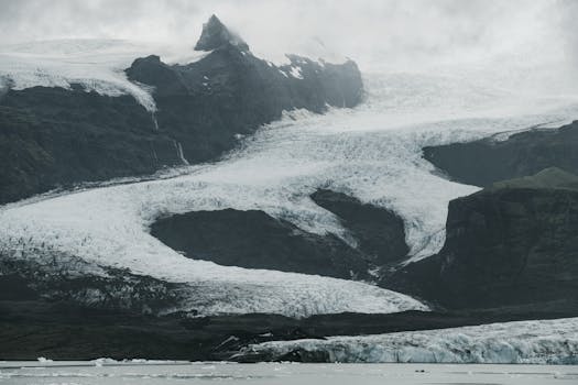Severe Nordic landscape of snowy mountain slopes covered with ice located near cold sea with black and white effect