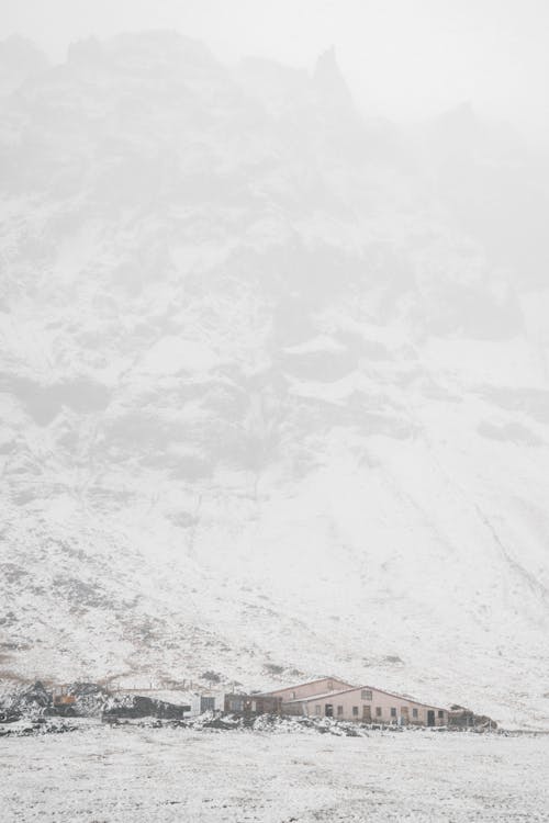 Fog over only house located at bottom of snowy mountain in overcast in winter evening