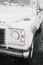 Range roving vehicle with lights on covered with frozen sleet parked on roadside in snowy day
