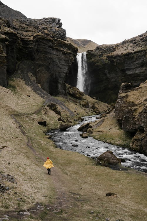 Unrecognizable traveler walking on mountain slope near waterfall