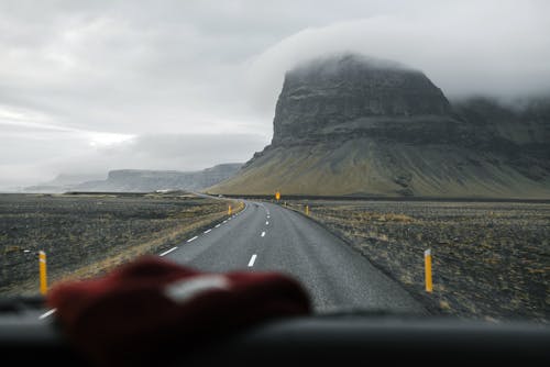 Through glass of empty asphalt road going through valley with mountain slopes against foggy sky