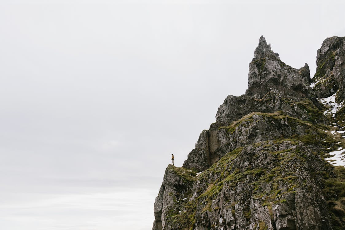 Free From below of unrecognizable hiker standing alone on edge of rocky cliff against cloudy sky Stock Photo