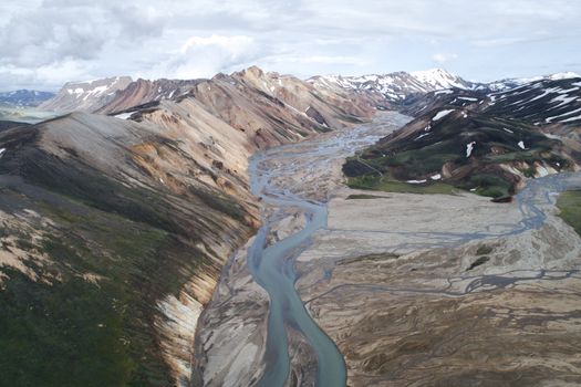 Drone view of scenic rhyolitic mountains in Iceland with muddy river flowing between mountain slopes
