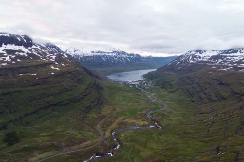 Free Spectacular aerial view of narrow river flowing into lake between green slopes of mountains with snow caps under overcast sky Stock Photo