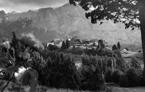 Black and white shot of modern remote village with contemporary decent buildings located amidst majestic mountains and lush abundant greenery