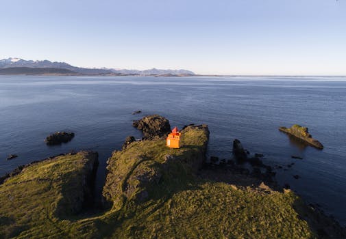 清晨的光线下，一座孤立的橙色灯塔矗立在岩石海岸线上，构成了一幅戏剧性的鸟瞰图