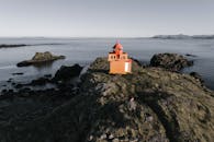 From above of lonely lighthouse keeper in warm clothes observing vicinities near small lighthouse on wild rocky seacoast