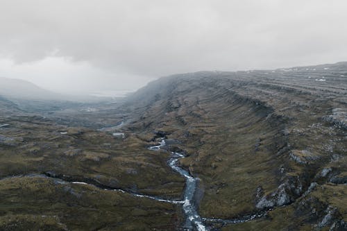 Mountainous terrain with small wild river in foggy day