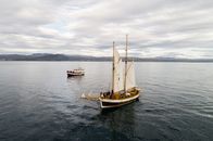 Beautiful modern sailing ship floating on sea surface near traditional fishing boat on cloudy day
