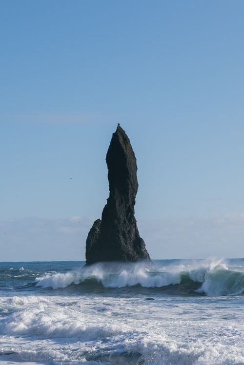 Free Huge black basalt stack rising from powerful wavy ocean against cloudless blue sky Stock Photo