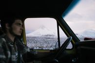 Man driving automobile along frozen field with mountains in distance