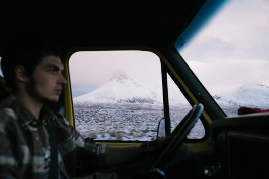 Man driving automobile along frozen field with mountains in distance