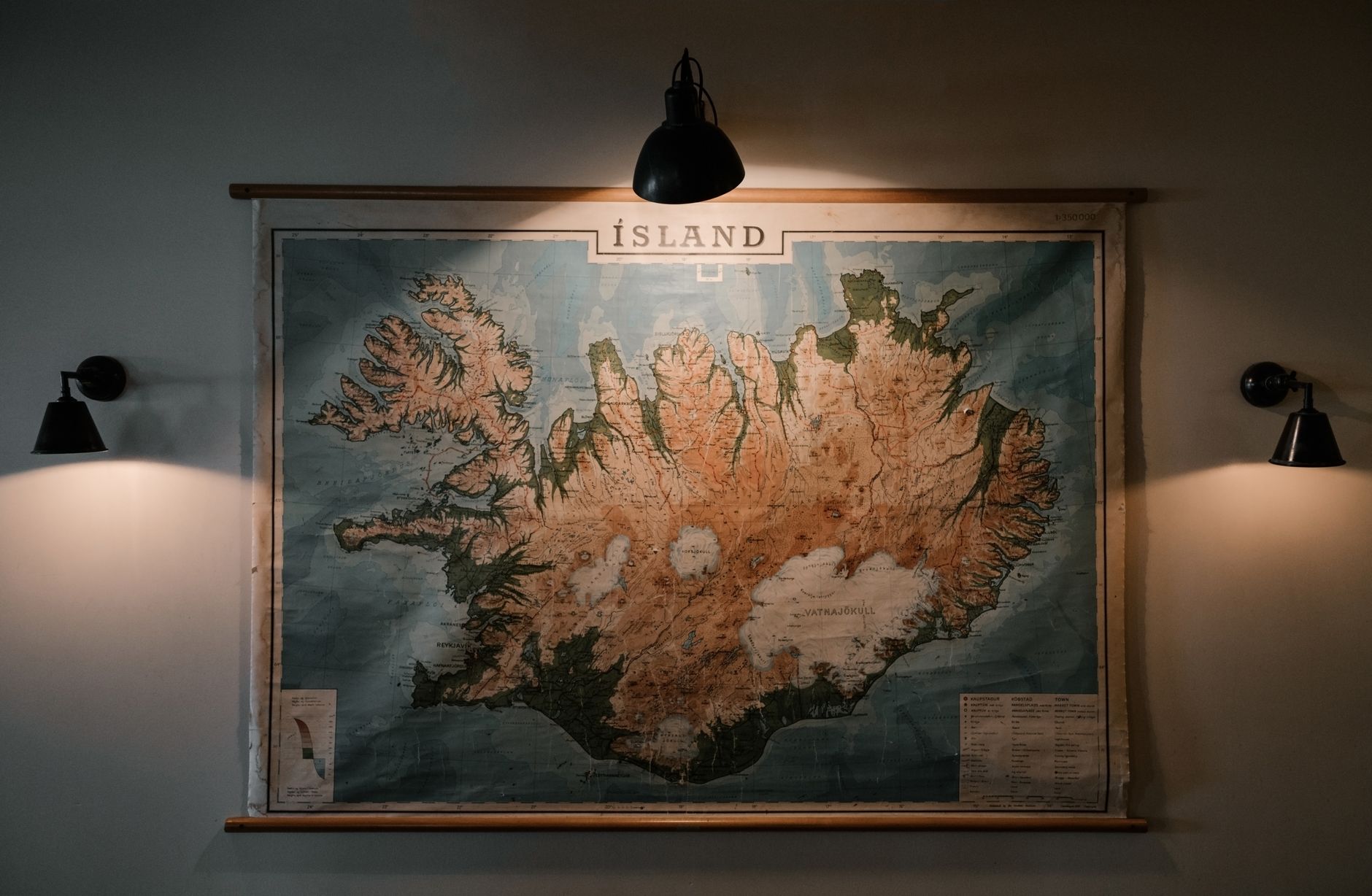 冰島環島導航大全:手機離線地圖與天氣警示要點 A vintage map of Iceland illuminated by warm lights on a museum wall