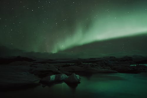 Dark stony terrain under starry night sky with amazing Aurora Borealis glowing with vibrant green color