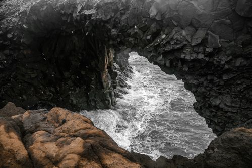 Free From above of breathtaking seascape of cliff with natural basalt rock arch on rough shore of sea Stock Photo