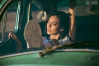 Serene young female in casual outfit laying back on car passenger front seat with arm raised and looking out window dreamily