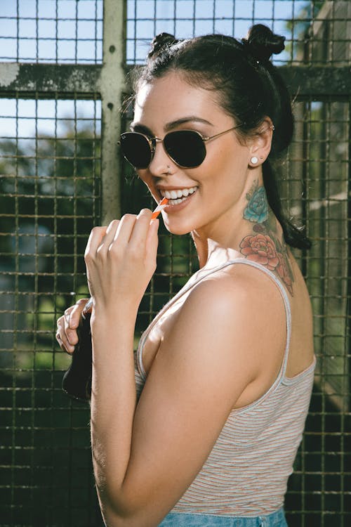 Tattooed woman in sunglasses standing against metal fence