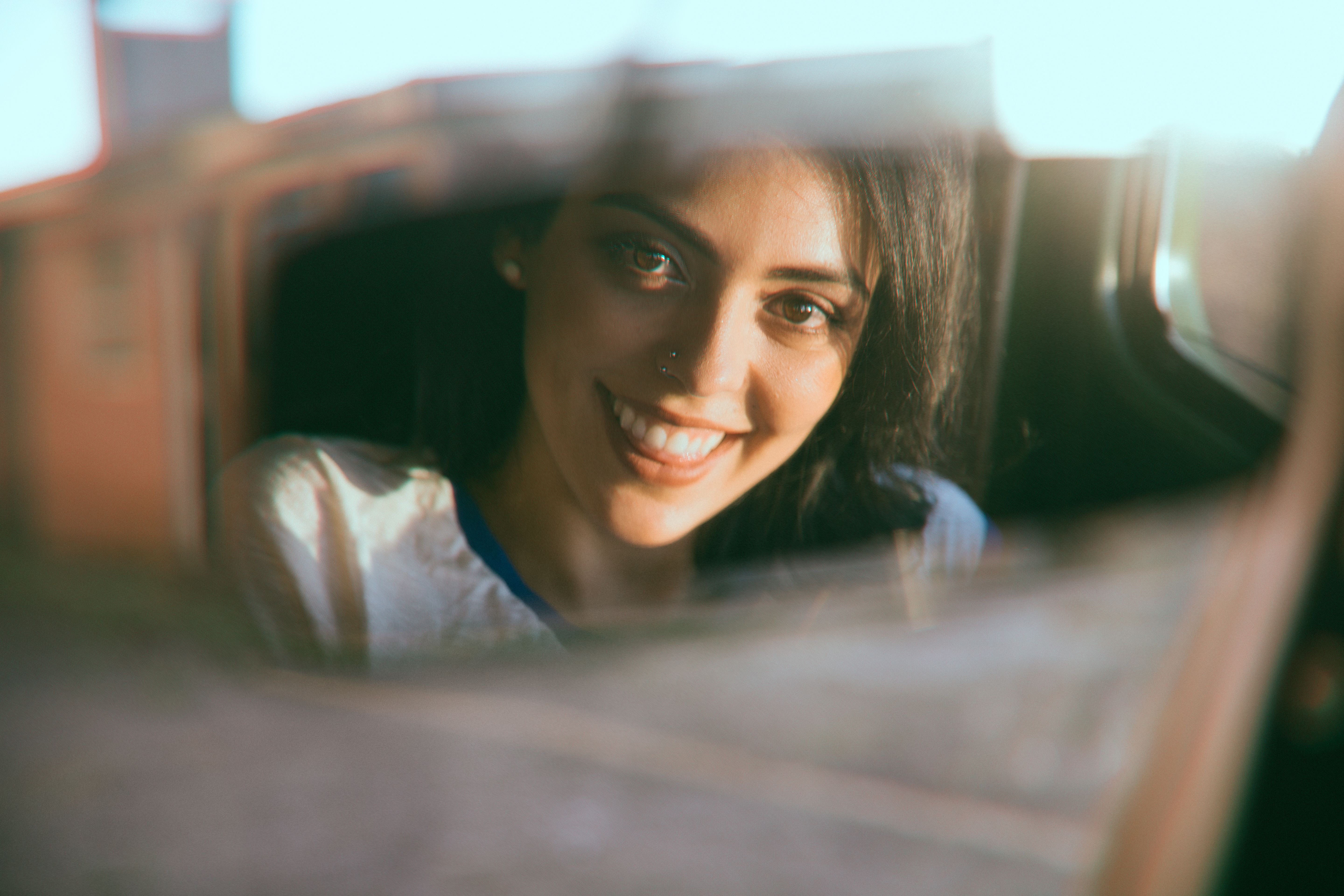 Positive young female with dark eyes and hair sitting in car and looking at mirror on summer day
