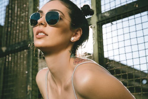Free Young woman in trendy sunglasses against metal fence Stock Photo