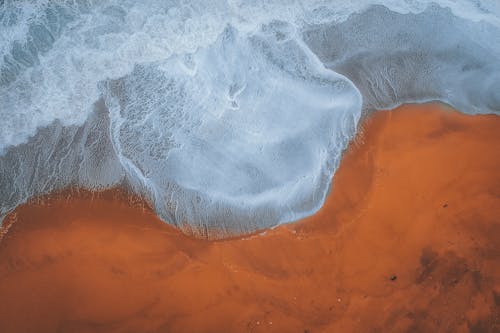 Free Drone view of foaming stormy clean sea waves rolling near brown sandy coastline Stock Photo