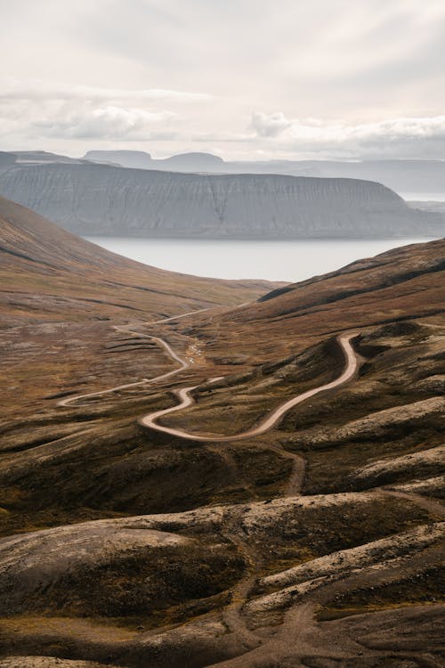 Picturesque view of windy road leading away to mountains ridge and lake in cloudy day