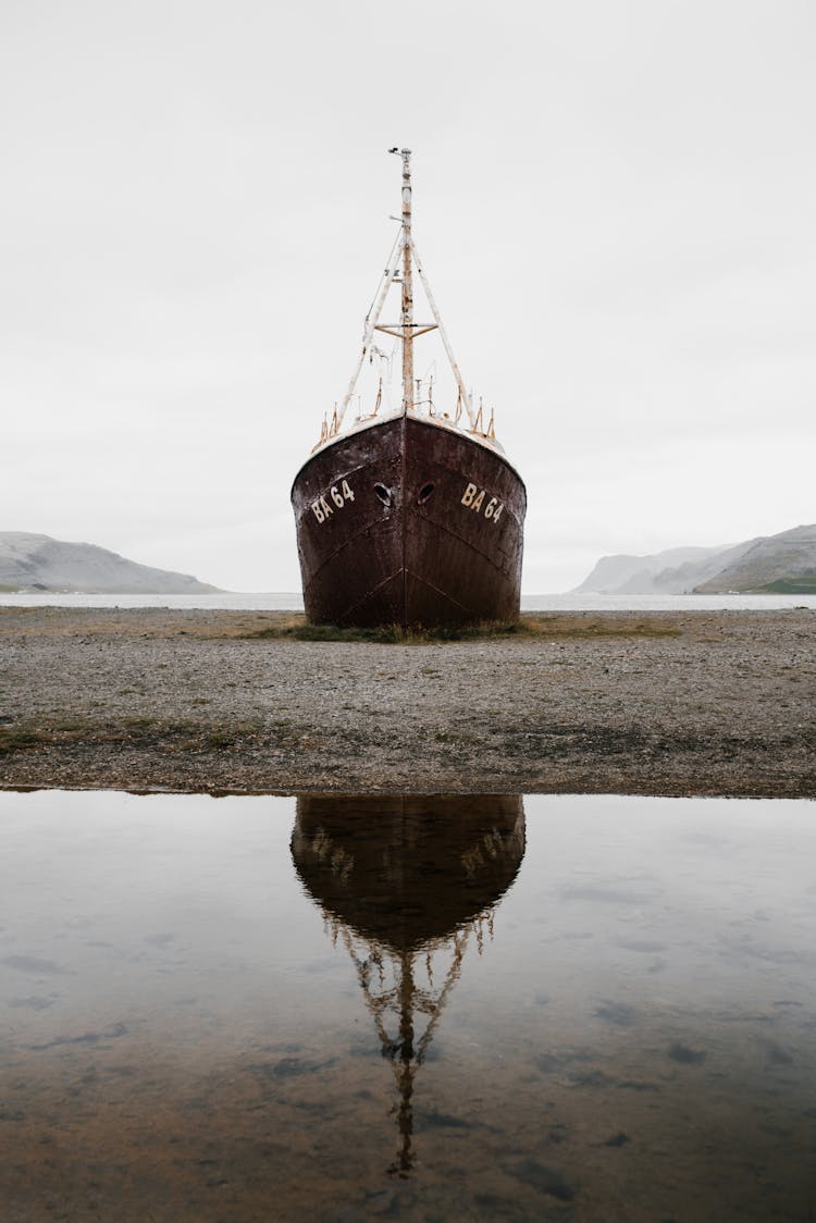 Old Vessel Stranded On Sandy Shore Near Mountains And Lake