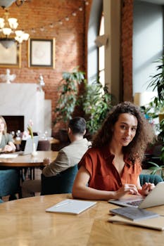 一位穿着红色衬衫的女性在时尚咖啡馆的砖墙边使用笔记本电脑