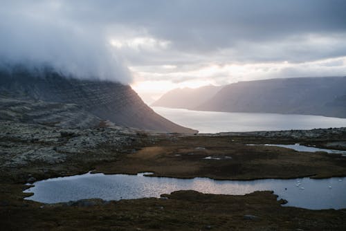 Lake surrounded by mountains in foggy weather at sundown