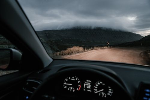 Free View from inside car on road in countryside near mounts and faded grass in mist under cloudy sky Stock Photo