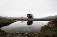 Group of tourists standing near old ship reflecting in pond