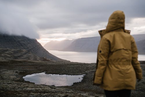 Faceless tourist standing near sea and mounts on foggy day