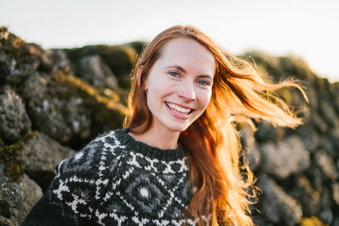 Positive ginger woman standing near stone wall in sunlight