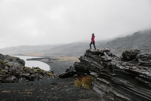 A Person Standing on Rock Formations during Foggy Weather