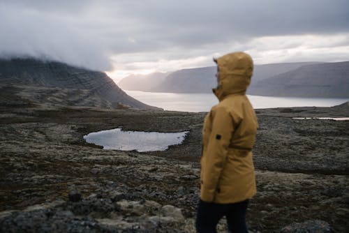 Unrecognizable tourist exploring mountains and lake in mist at sunset