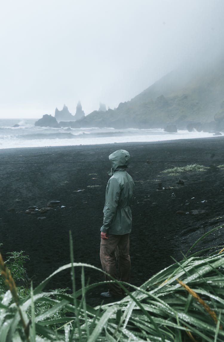 Unrecognizable Tourist Standing Near Ocean And Mount On Rainy Day