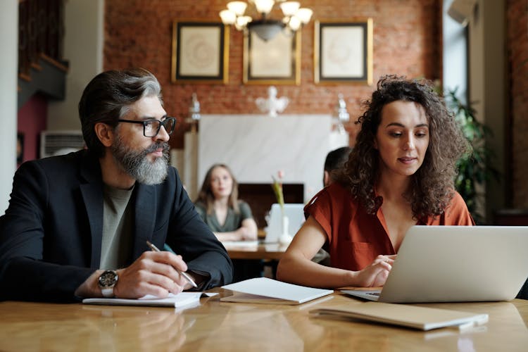 Man Taking Notes And Woman Scrolling On A Laptop