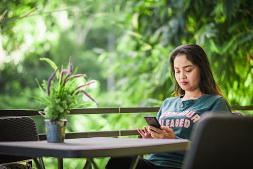 Concentrated young female freelancer browsing cellphone while working remotely in green outdoor terrace