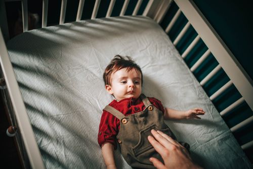 Free From above of faceless person pulling hand to child resting in crib in kids room Stock Photo