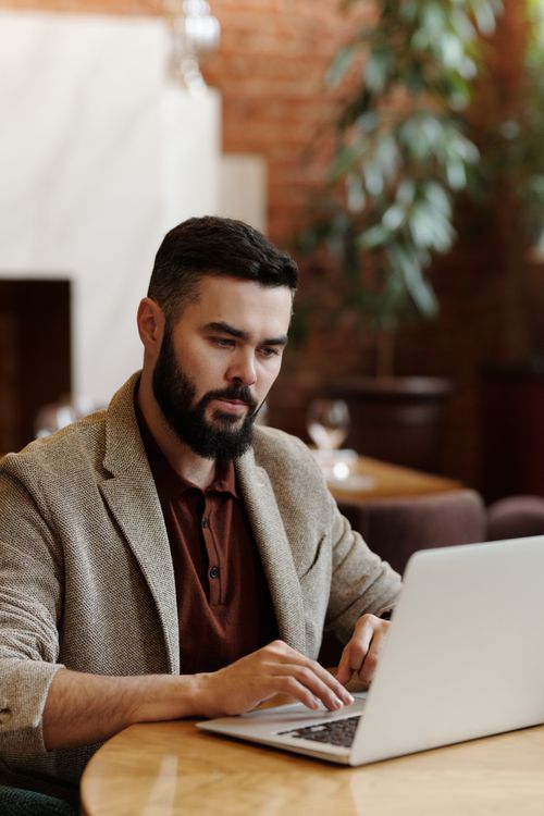 Free Bearded man working intensely on a laptop in a stylish, modern cafe setting. Remote work concept. Stock Photo