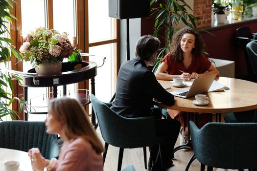 Two professionals engaged in a meeting at a stylish café with laptops and coffee.