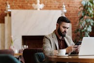 一位大胡子男人在时尚的咖啡店里用智能手机和笔记本电脑远程工作