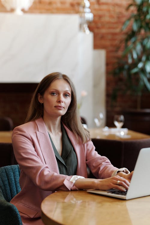 Woman in Pink Blazer Sitting on Chair Using Laptop