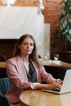 Confident woman working remotely on laptop in stylish cafe setting.