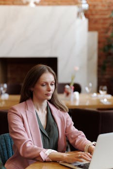 Professional woman in a cafe working on a laptop, showcasing modern telecommuting.
