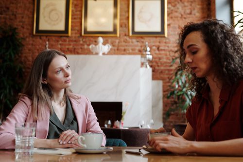 Free Two women engaged in serious discussion over coffee in a cozy indoor café setting. Stock Photo