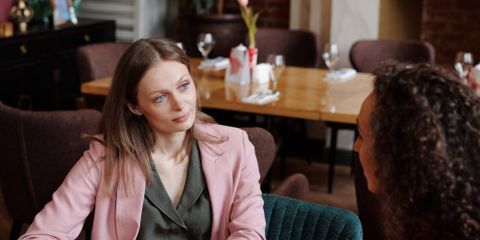 Two women having a thoughtful conversation in a cozy café setting, discussing over coffee.