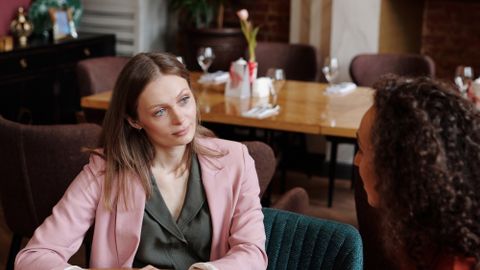 Two women having a thoughtful conversation in a cozy café setting, discussing over coffee.